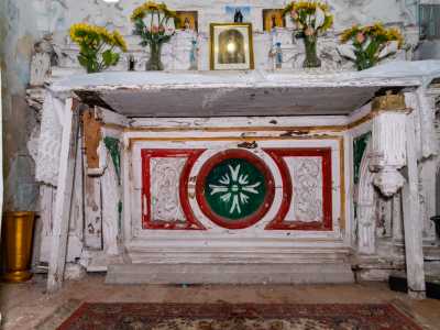 Al centro il grazioso altare in legno, ricco di immaginette sacre e vasetti di fiori, mostra nella base eleganti elementi ricolorati nel tempo con toni rosso, verde e dorato coperti da una bianca tovaglia ricamata